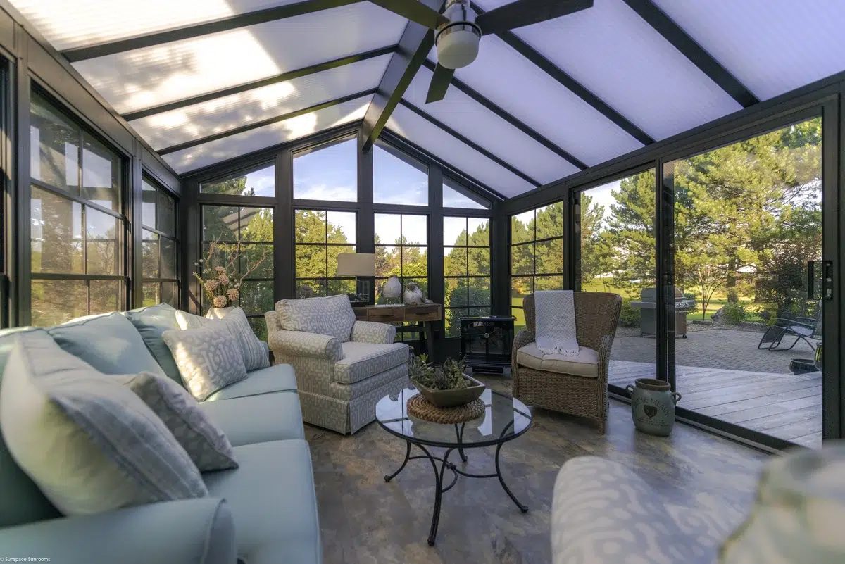 Finished Sunspace sunroom with dark frames, couches and a view out to the deck and trees